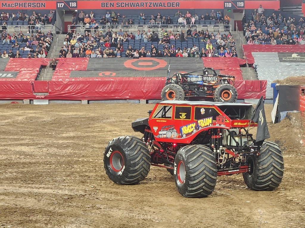 A photo of Krazy Train, a popular Monster Truck, and the audience watching on, with Terminal Velocity, another car, in the background.
