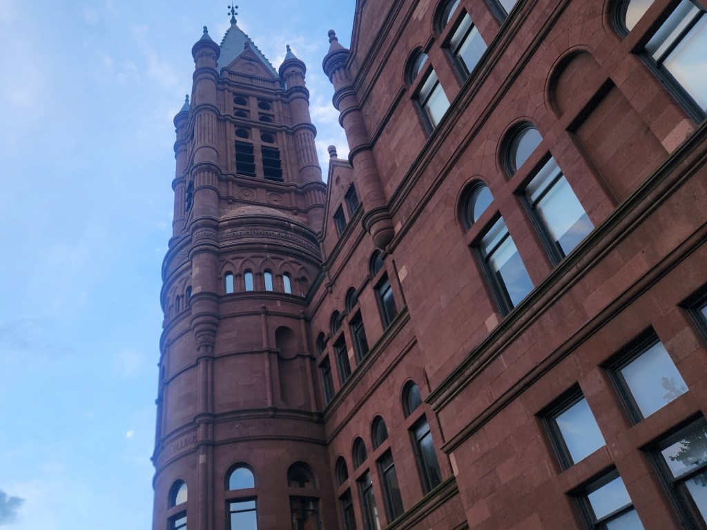 My own photo of Crouse College, located in Syracuse, New York, taken at an angle where the peak of the college looms above you. I was there visiting and was struck by the color of the rust-red bricks and the rather gothic architecture of the college.