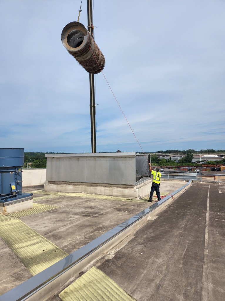 A man named Keith guides a large drum into a room, to replace a piece of a paper mill.